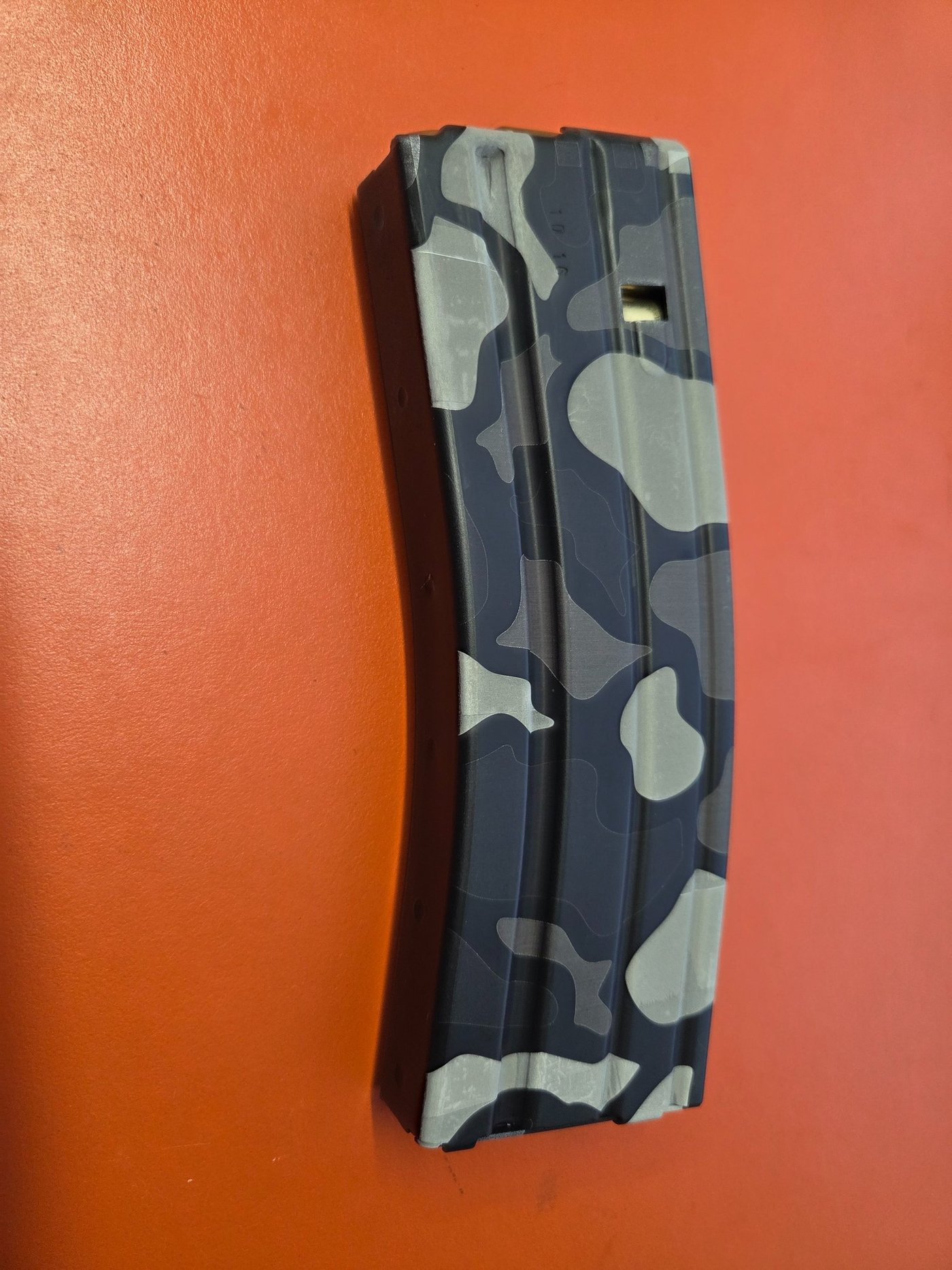 A rifle magazine in blue-grey camouflage, fiber-engraved down its length.
