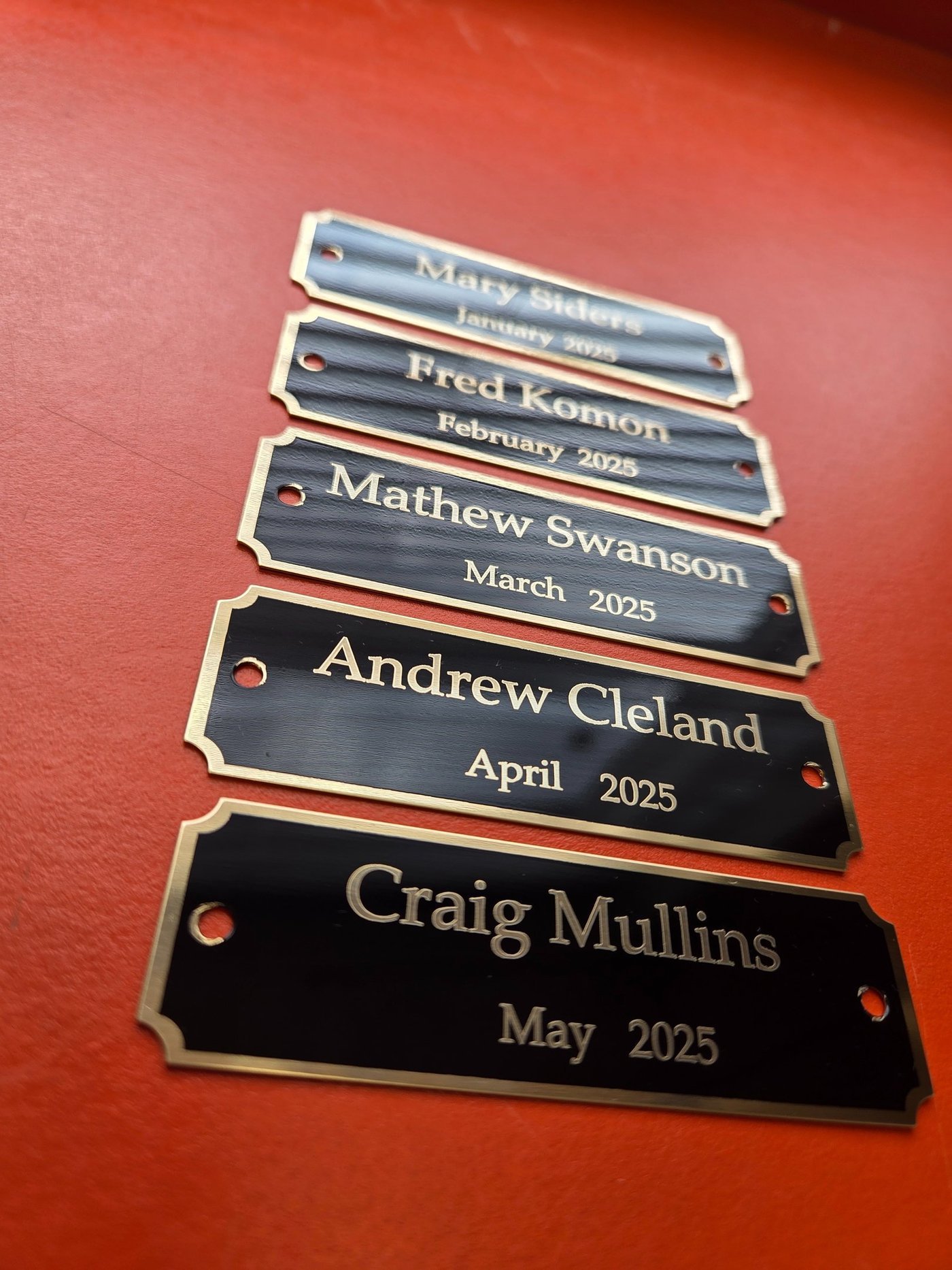 A set of metal name plates engraved with names and months, made for an employee recognition board.