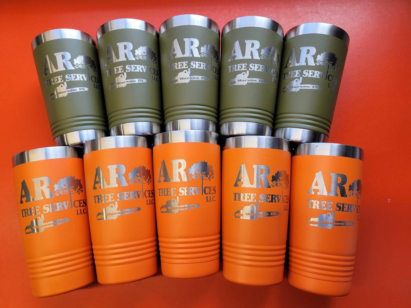 A large batch of olive and orange tumblers, all engraved with the AR Tree Services logo.