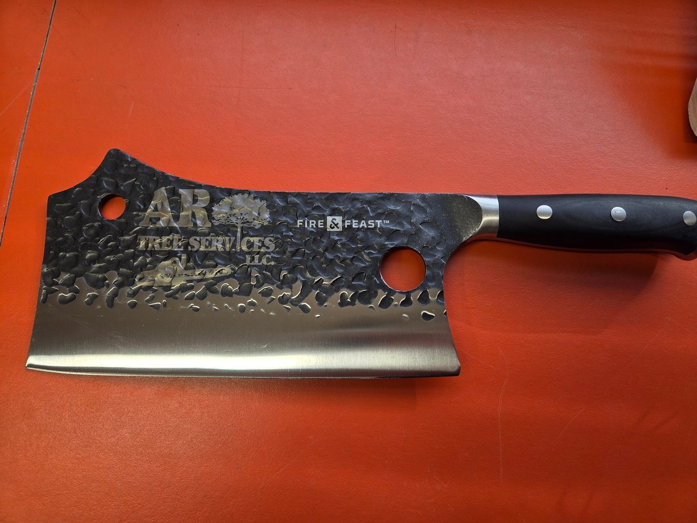 A hammered steel cleaver fiber-engraved with the AR Tree Services Fire and Feast logo.
