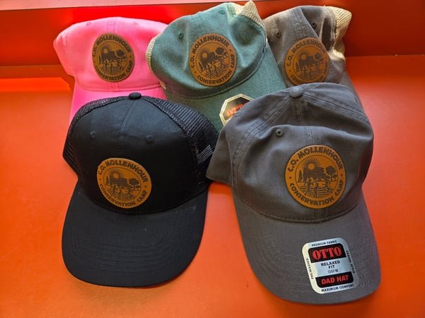 Five caps in pink, green, grey, black and charcoal, each with a round leather patch engraved with a conservation camp crest.