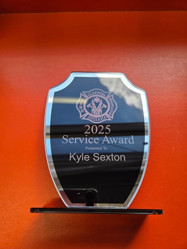 A clear acrylic shield award engraved with a fire department crest reading 2025 Service Award presented to Kyle Sexton.