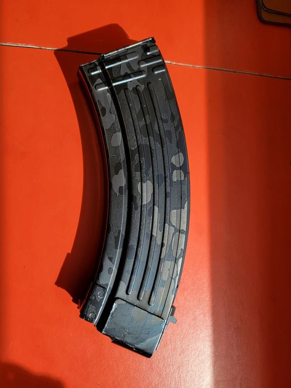 A rifle magazine with a camouflage finish, fiber-engraved along its curved body.
