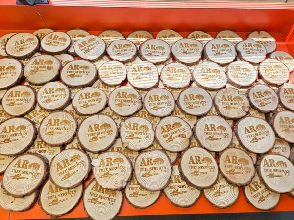 Dozens of round wood-slice ornaments, each engraved with the AR Tree Services logo.