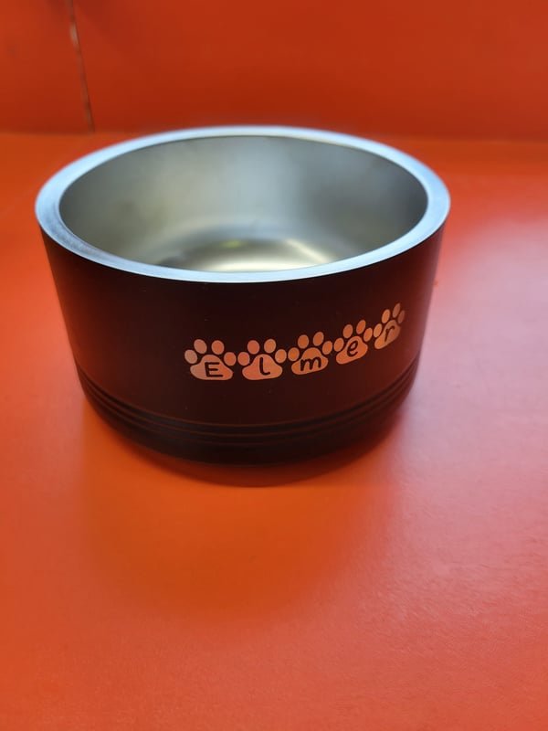 A black powder-coated pet bowl engraved with the name Elmer spelled out between paw prints.