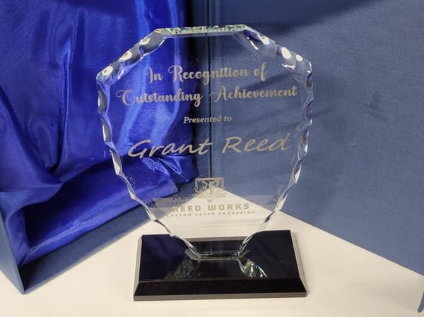 A faceted glass award on a black base engraved In Recognition of Outstanding Achievement, presented to Grant Reed.