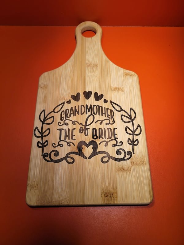 A bamboo paddle board engraved with a decorative heart wreath reading Grandmother of the Bride.