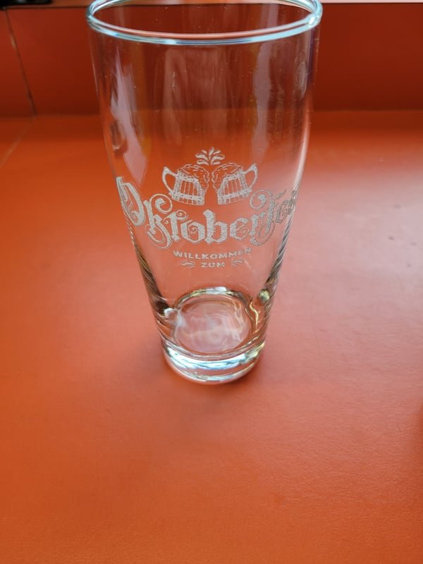 A tall pint glass etched with an Oktoberfest Willkommen design.