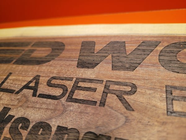 A close-up of a walnut sign with the words Reed Works Laser Engraving cut deeply into the grain.