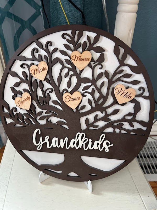 A round cut wooden family tree hung with small engraved name hearts above the word Grandkids.