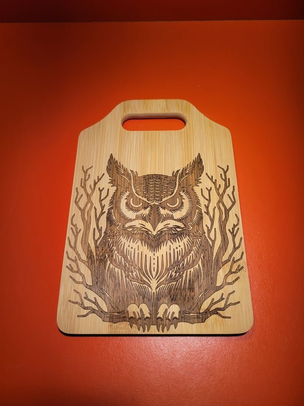 A bamboo cutting board engraved with a detailed owl perched among bare branches.