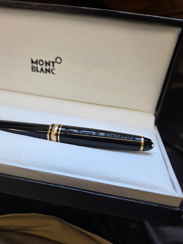 A black and gold Montblanc pen in its presentation case, fiber-engraved along the barrel.