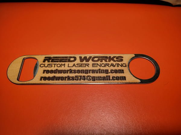 A wooden bottle opener engraved with the Reed Works name, website and email.
