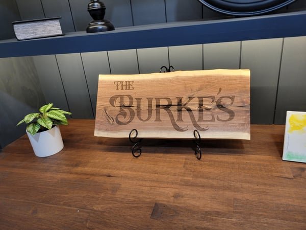 A live-edge wood family name sign reading The Burke's displayed upright on a stand.