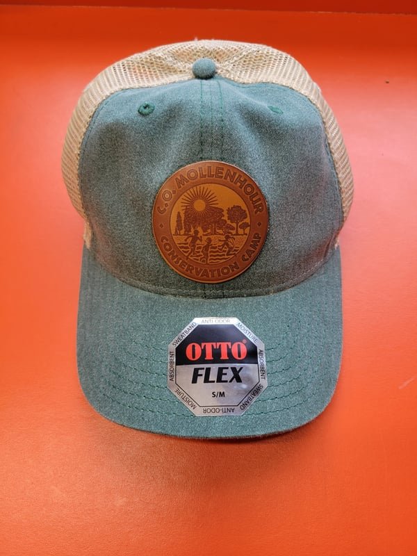 A grey cap with a round leather patch engraved with the C.O. Mollenhour Conservation Camp crest.