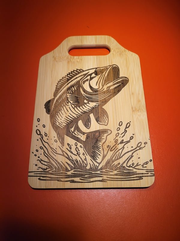 A bamboo cutting board engraved with a largemouth bass leaping from water.