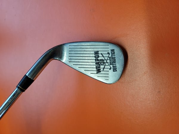 A golf club wedge with its face fiber-engraved with a Weapon of Mass Destruction design.