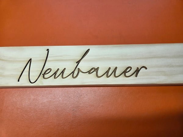 A pale wood sign engraved in large flowing script with the family name Neubauer.