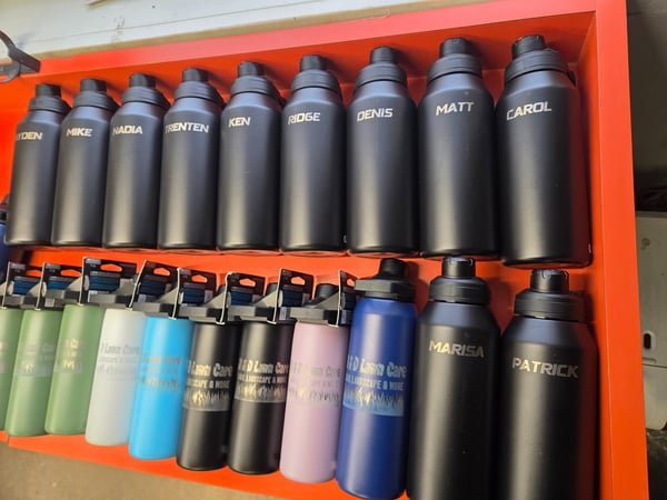 Rows of black and pastel insulated bottles, each engraved with an individual staff name.