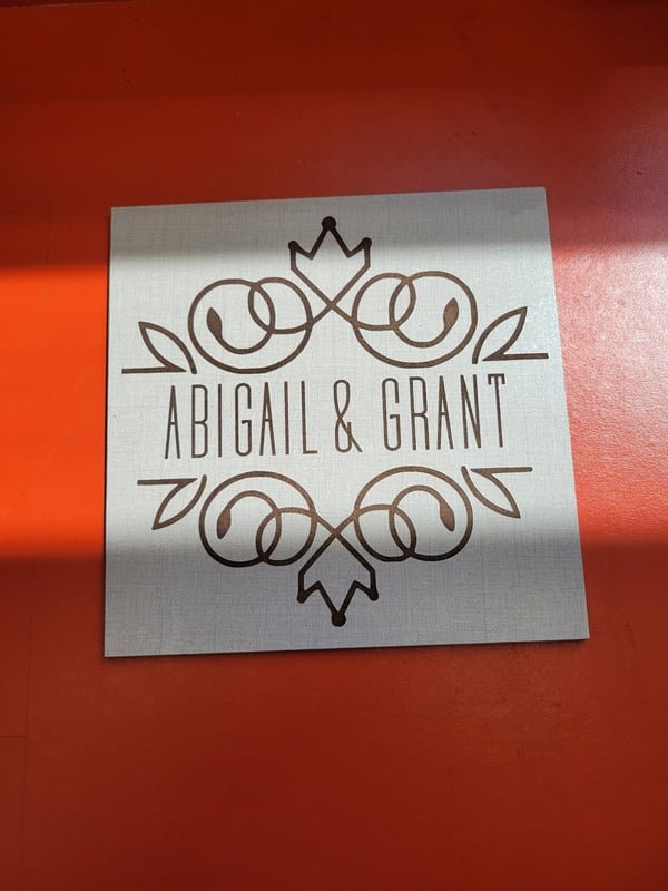 A brushed metal plate engraved with a decorative scroll and the names Abigail and Grant.
