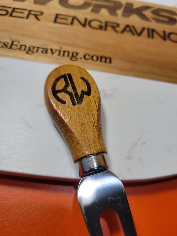 A cheese knife with a wooden handle engraved RW, resting on a marble serving board.