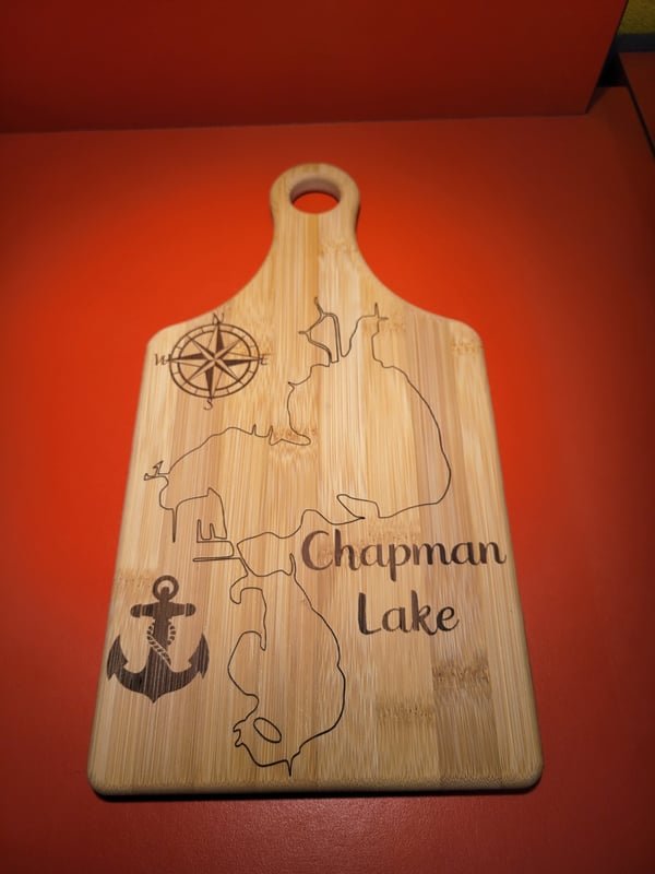 A bamboo paddle board engraved with a map of Chapman Lake, a compass rose and an anchor.