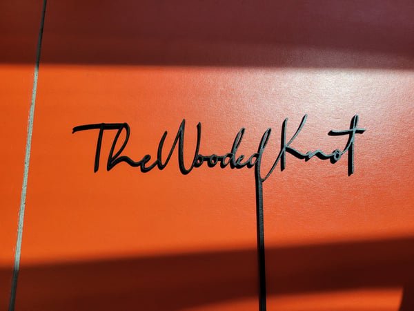 A black acrylic cake topper cut in script reading The Wooded Knot.