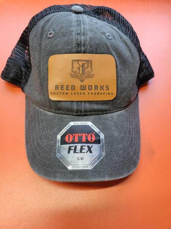 A charcoal trucker cap with a leather patch engraved with the Reed Works logo.