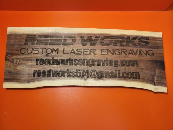 A live-edge wood sign engraved with the Reed Works name, website and email address.