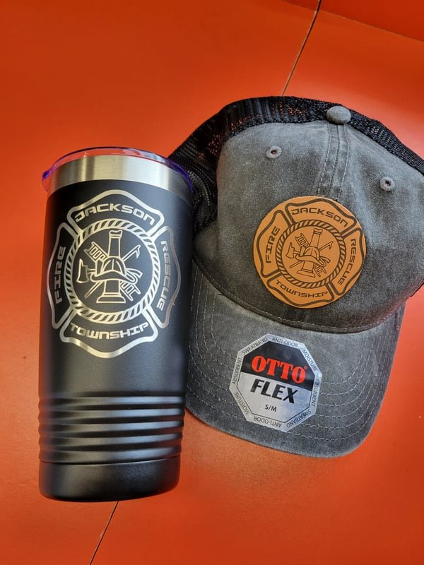 A black tumbler and a grey leather-patch cap, both carrying the Jackson Township Fire crest.