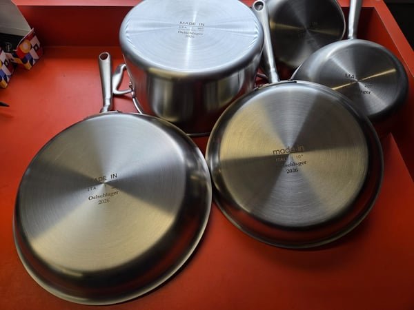 A set of stainless steel pans, their bases fiber-engraved with the name Oelschlager and the year 2026.