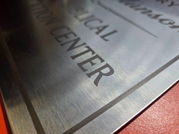 A close-up of a brushed metal sign showing deeply engraved lettering.