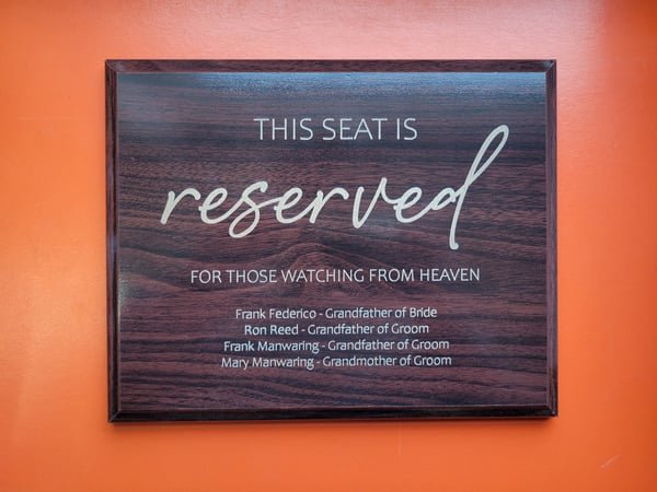 A dark plaque engraved This Seat Is Reserved For Those Watching From Heaven, listing four grandparents.