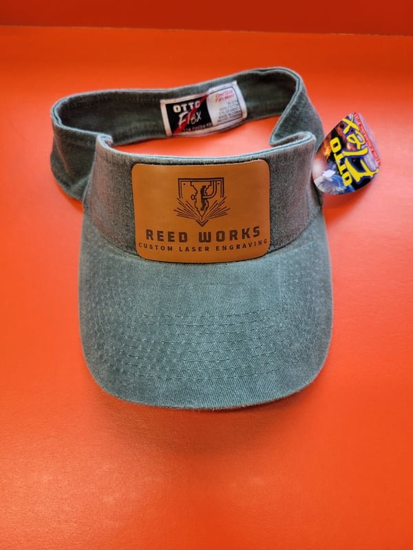 A teal visor with a leather patch engraved with the Reed Works logo.