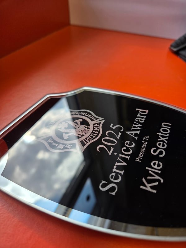 A black mirrored acrylic award engraved with a fire crest reading 2025 Service Award presented to Kyle Sexton.