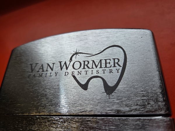 A brushed metal plate engraved with the Van Wormer Family Dentistry tooth logo.