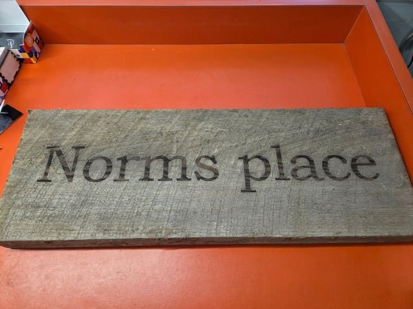 A weathered barn-wood sign engraved with the words Norms place.