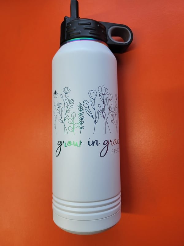 A white bottle engraved with a delicate wildflower spray and the words Grow in grace.
