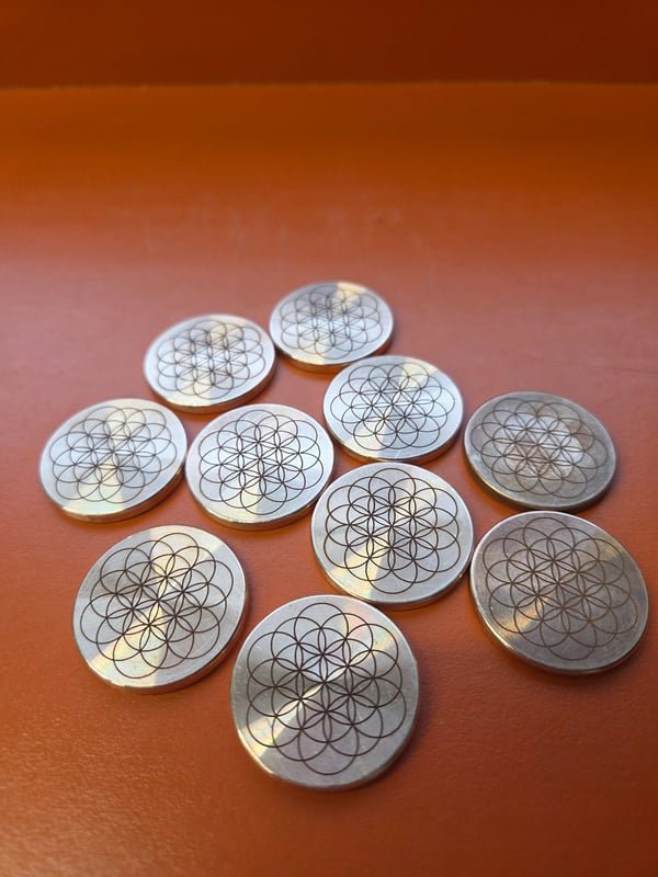 A group of stainless discs fiber-engraved with a fine Flower of Life geometric pattern.