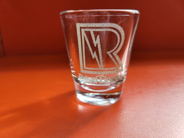 A shot glass etched with the Reed Works R lightning logo.