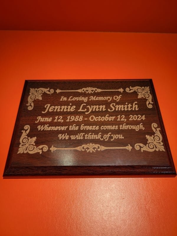 A wood plaque engraved In Loving Memory Of Jennie Lynn Smith with her dates and a remembrance verse.