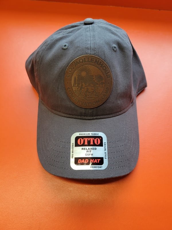 A grey dad hat with a round leather patch engraved with the Mollenhour camp crest.