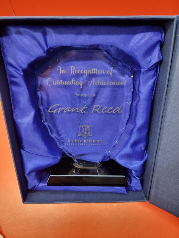 A faceted glass award in a blue presentation box, engraved In Recognition of Outstanding Achievement.