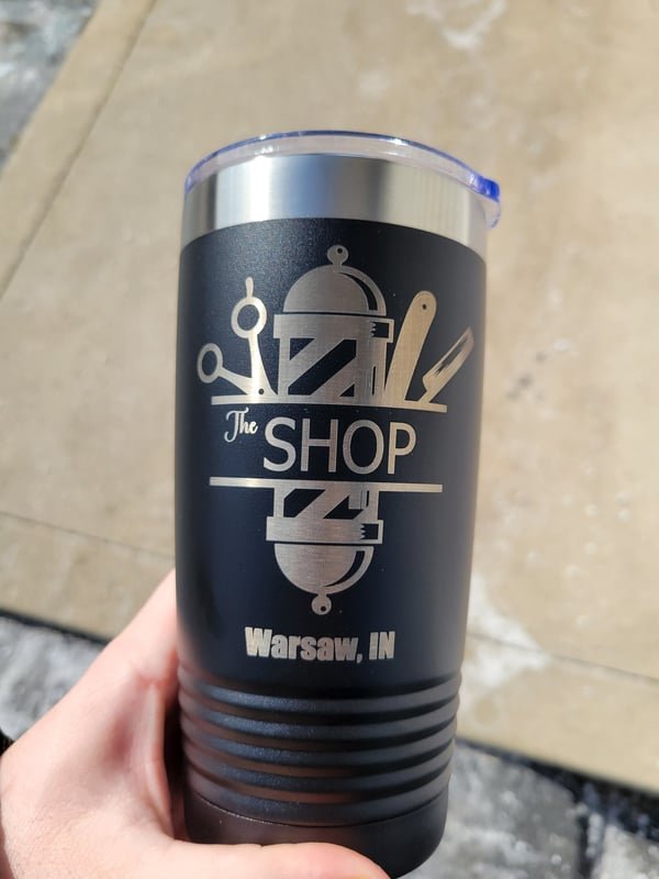 A black tumbler engraved with a barber pole, scissors and razor above The Shop, Warsaw, IN.