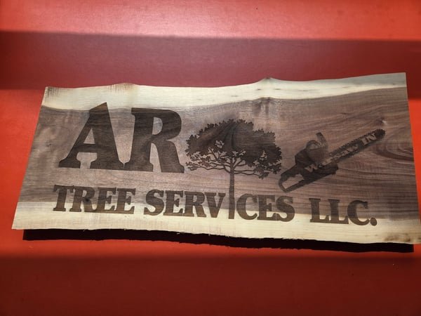 A live-edge wood sign engraved with the AR Tree Services LLC logo and chainsaw.