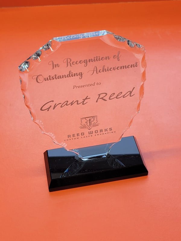 A faceted glass award on a black base engraved In Recognition of Outstanding Achievement, Grant Reed.