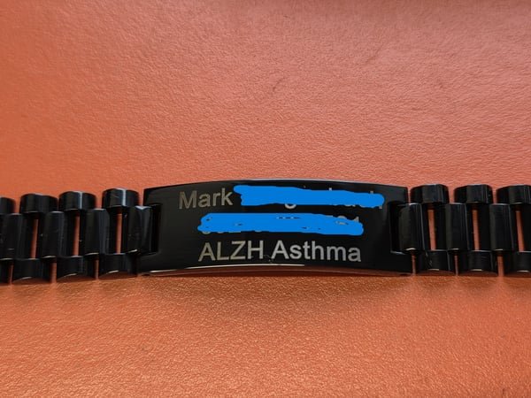 A black stainless medical alert bracelet fiber-engraved with a name and medical conditions.