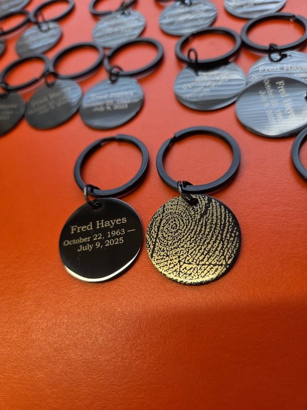 Memorial keyrings pairing an engraved name tag with a gold disc bearing a fingerprint.