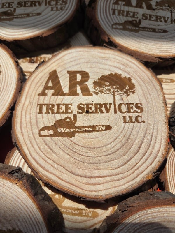 Stacked wood slices engraved with the AR Tree Services logo, tree and chainsaw.