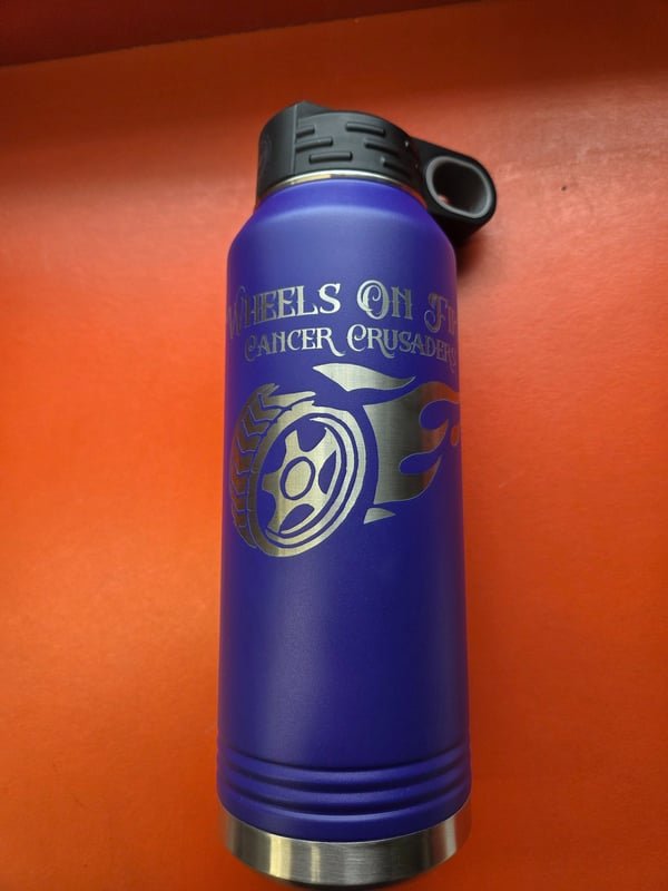 A blue bottle engraved with the Wheels On Fire Cancer Crusaders flaming-wheel logo.